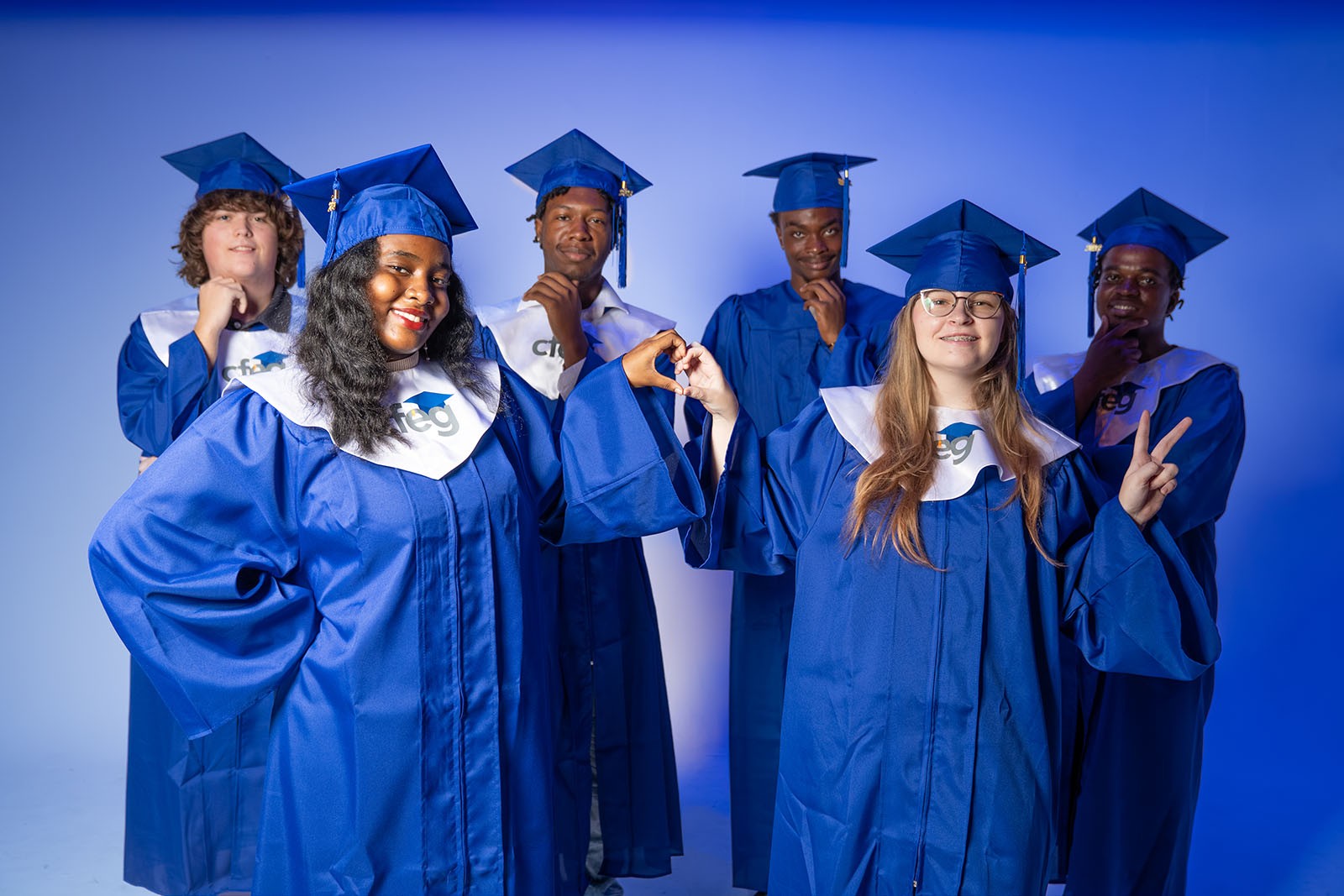 Six CFEG graduates in blue caps and gowns with white CFEG-branded stoles, posing together after commencement.