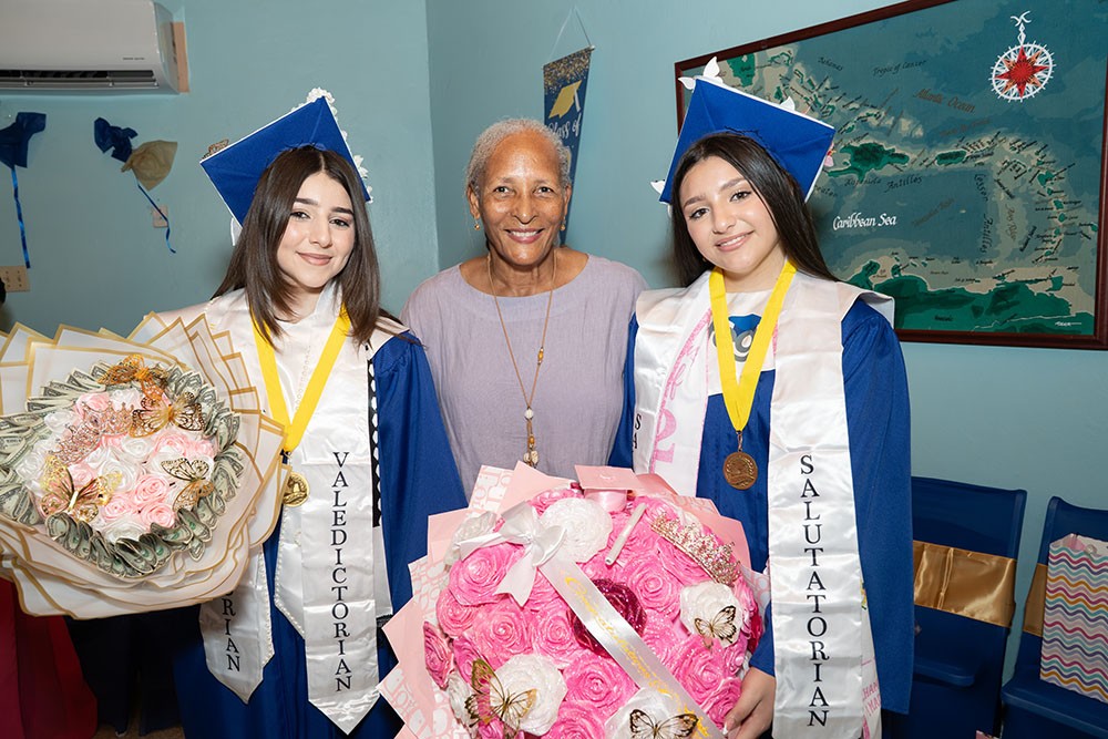 CFEG&rsquo;s Valedictorian and Salutatorian in caps and gowns, wearing their honor stoles and medals, with a family member.