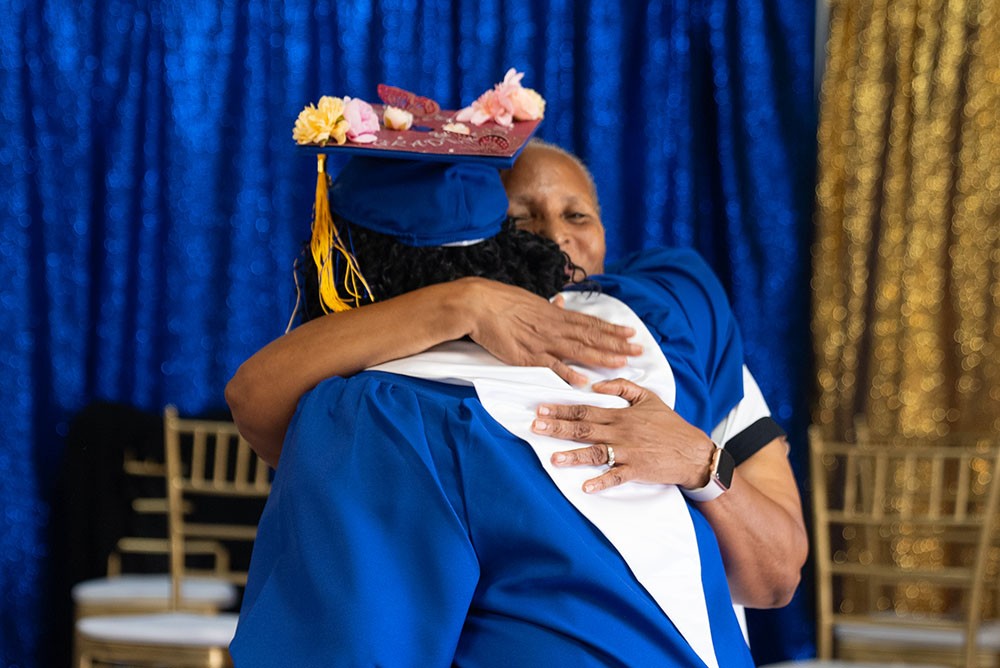 A CFEG graduate in a flower-decorated cap embracing a family member on stage.